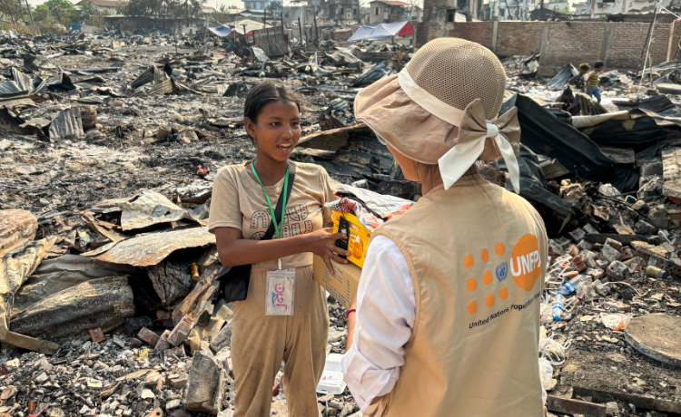 Une jeune femme debout au milieu de gravats parle avec une femme portant un chapeau et un gilet portant le logo de l’UNFPA