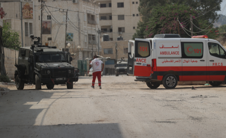 مسعف من جمعية الصليب الأحمر الفلسطيني يقف على الطريق أمام سيارة جيب تابعة للجيش الإسرائيلي.