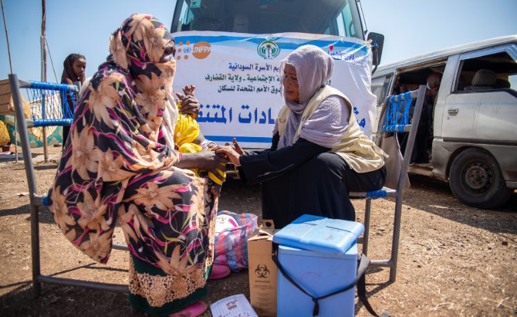 A Une femme est assise dehors pour sa consultation avec une membre de l’équipe de santé mobile de l’UNFPA.